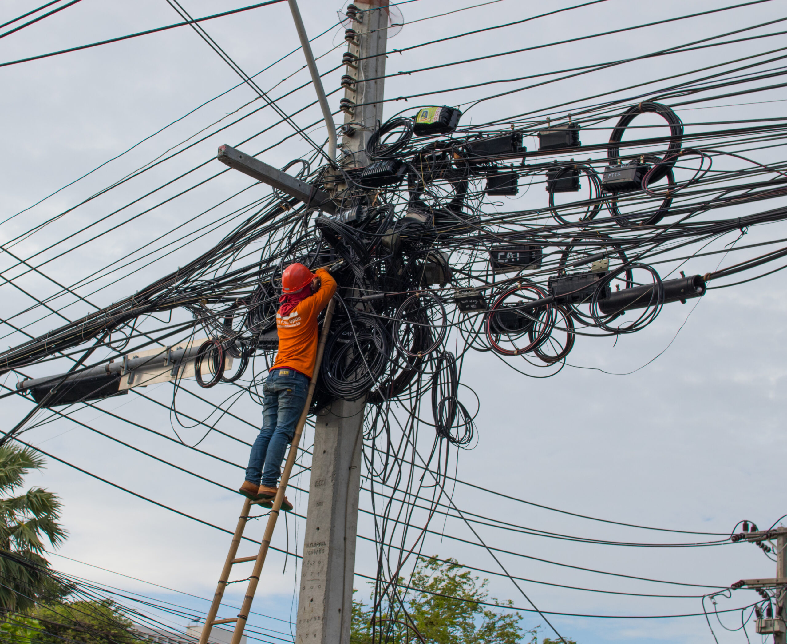 Worker attempting to organize a chaotic mess of overhead wires on a utility pole.
